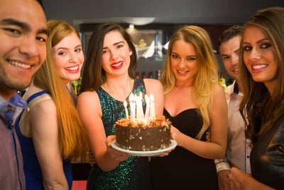 Happy friends celebrating brithday one holding birthday cake looking at camera in a nightclub