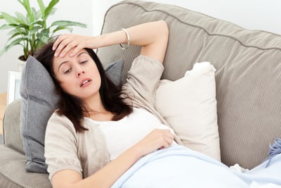 Indisposed woman feeling her temperature while resting on the sofa at home