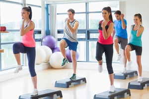 Full length of instructor with fitness class performing step aerobics exercise in gym