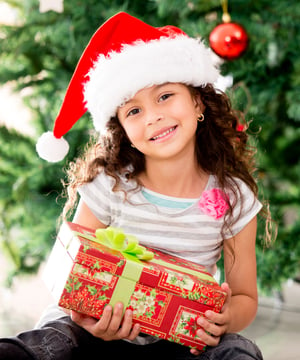 Little girl sitting by the tree holding a Christmas gift