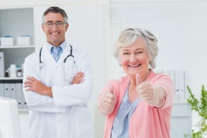 Portrait of happy female patient showing thumbs up sign while standing with doctor in clinic