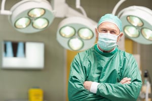 Smiling surgeon crossing his arms while standing in a surgical room